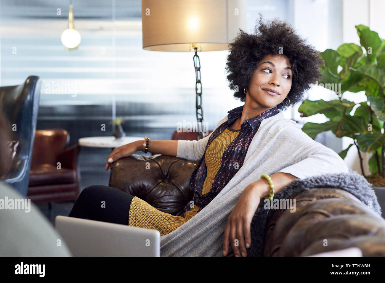 Geschäftsfrau blickt weg, während sie im kreativen Büro auf dem Sofa sitzt Stockfoto