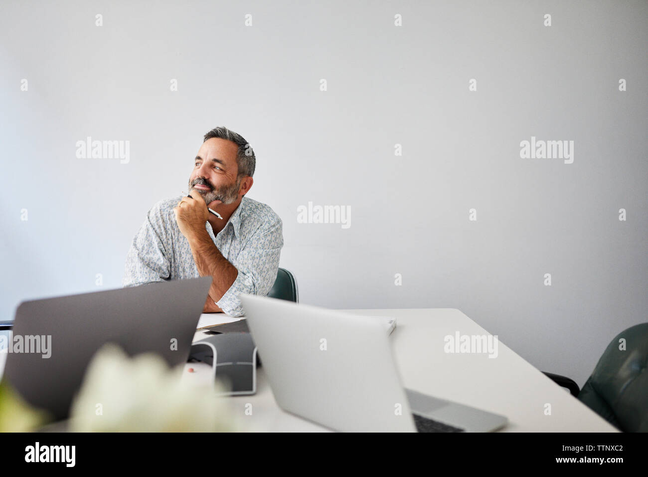 Nachdenklich Geschäftsmann mit der Hand am Kinn sitzen gegen Mauer am Konferenztisch im Board Room Stockfoto