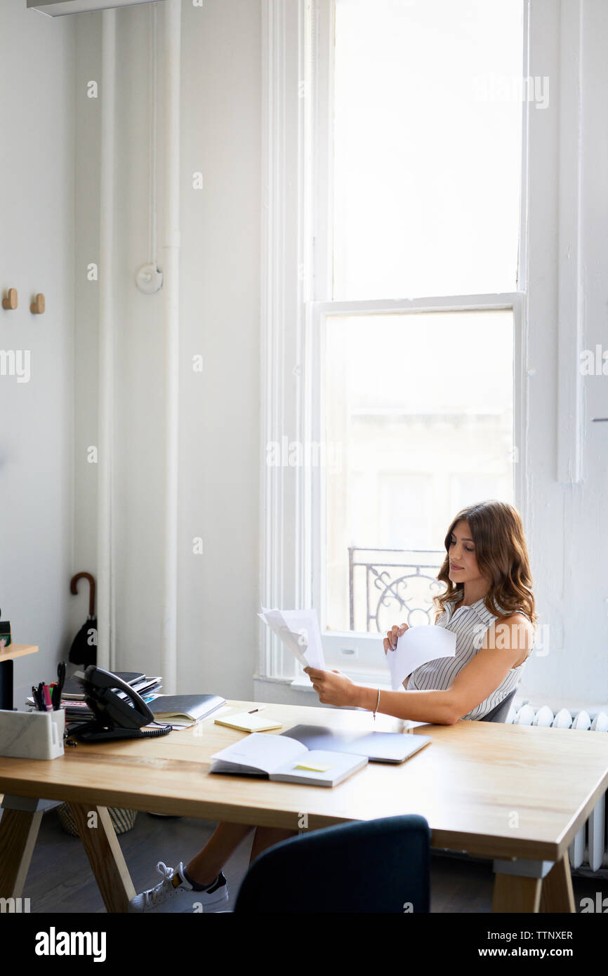 Geschäftsfrau, die Dokumente untersucht, während sie am Schreibtisch im Büro sitzt Stockfoto