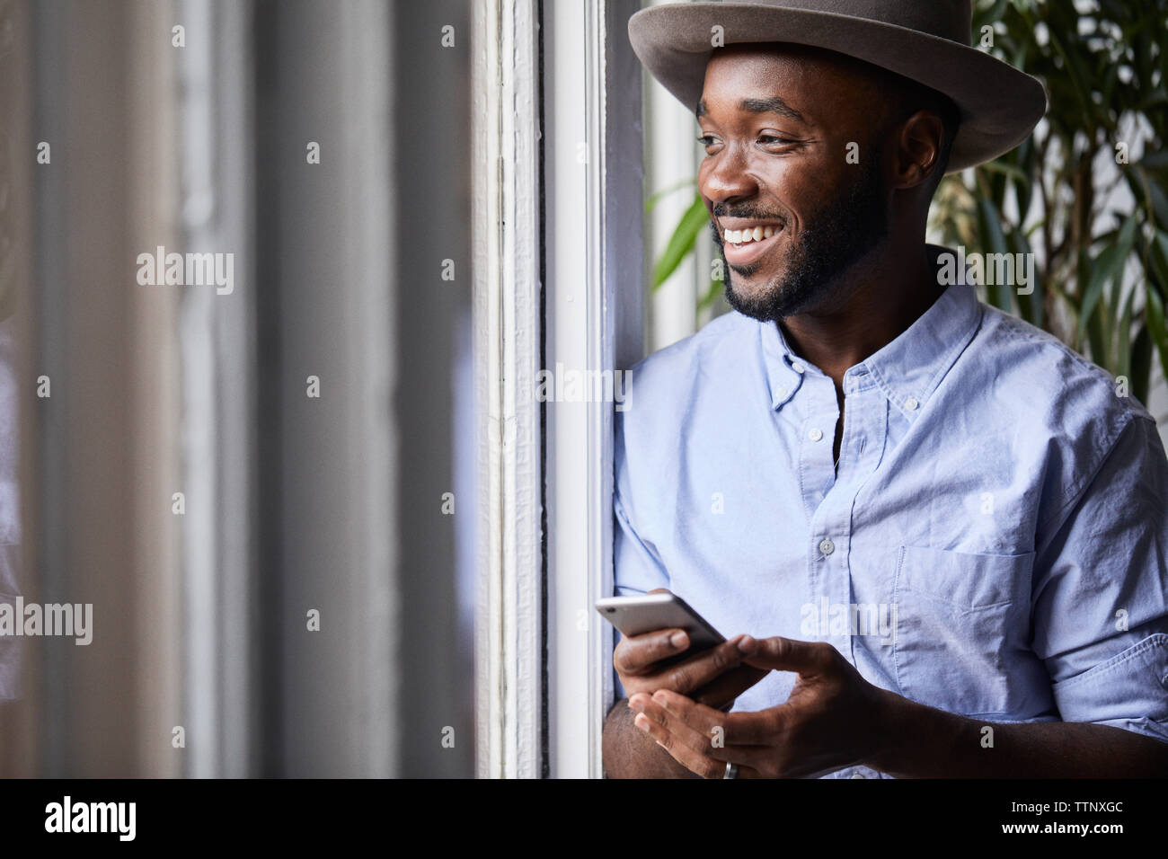 Lächelnd Geschäftsmann mit Smart Phone im Stehen durch Fenster in kreative Büro Stockfoto