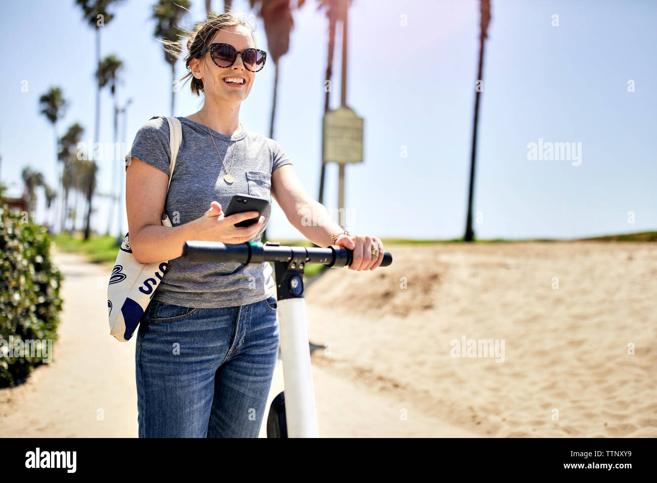 Frau mit Handy stehen auf elektrische push Roller am Strand an einem sonnigen Tag Stockfoto