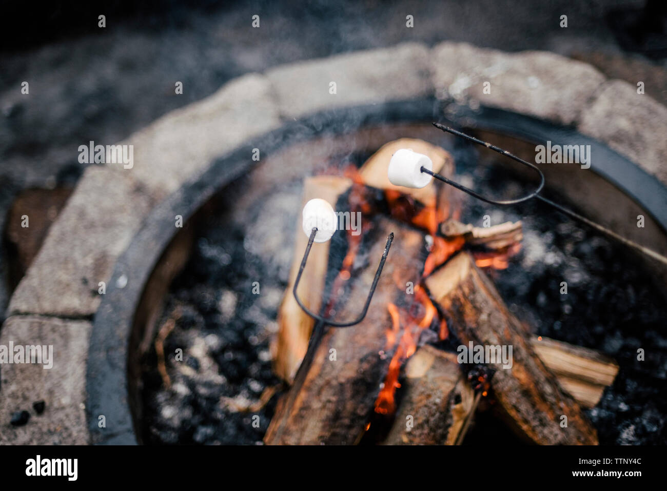 Hohe Betrachtungswinkel und Marshmallows geröstet über brennende Feuergrube Stockfoto