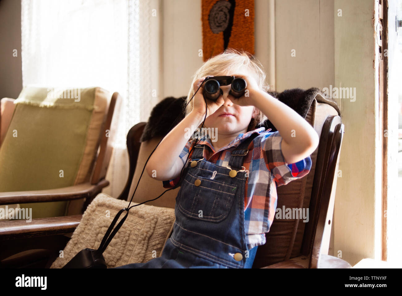 Junge Blick durch ein Fernglas während auf Stuhl zu Hause sitzen Stockfoto