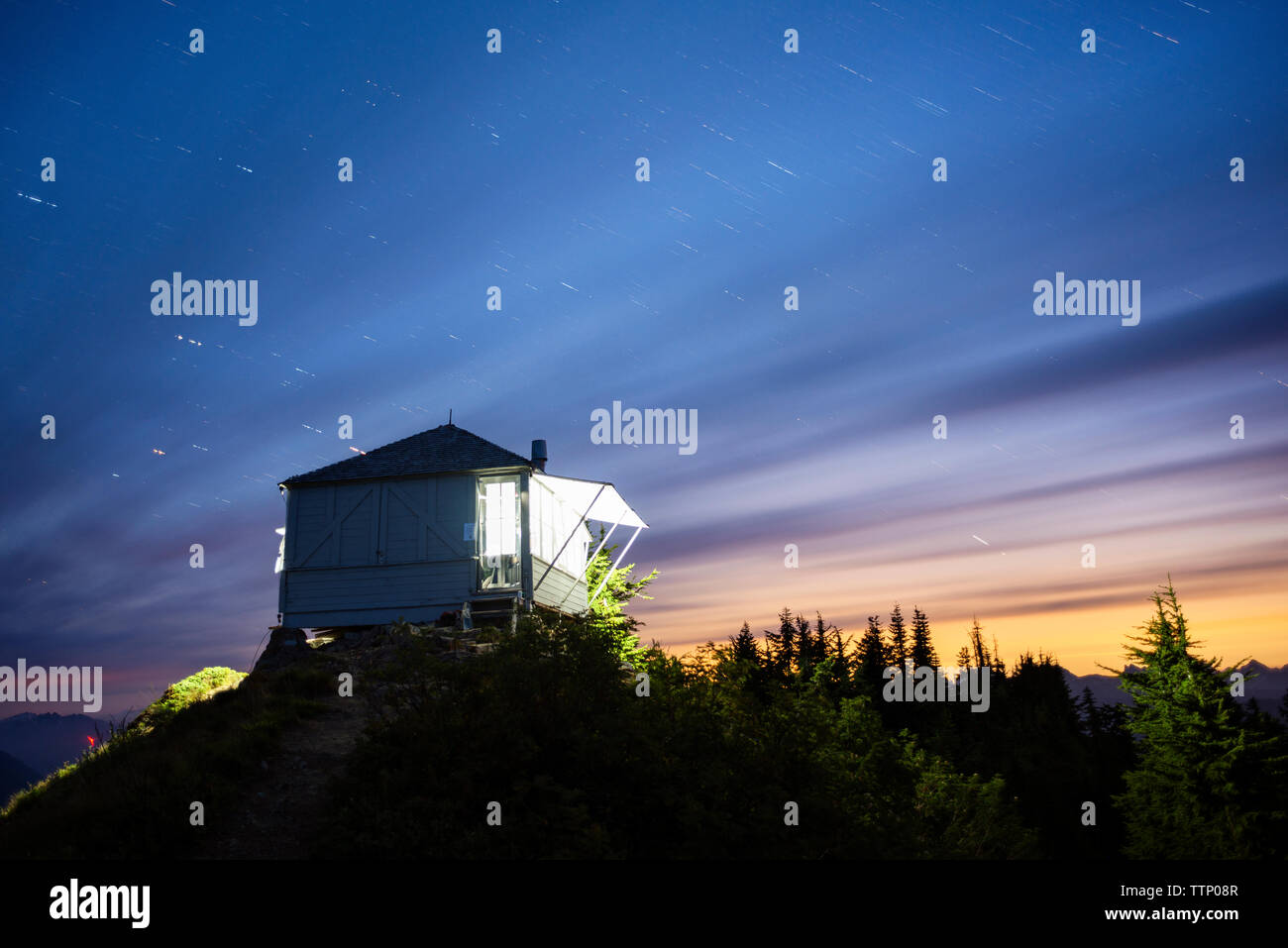 Beleuchtete Häuschen auf dem Berg gegen bewölkter Himmel bei Nacht Stockfoto