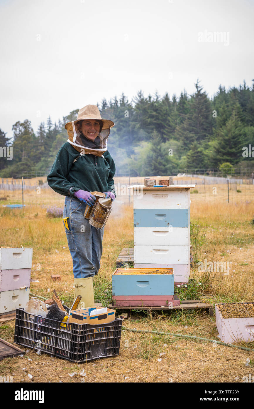 Portrait von weiblichen Imker Tragen von Arbeitskleidung im Stehen durch die Bienenstöcke auf der Farm Stockfoto