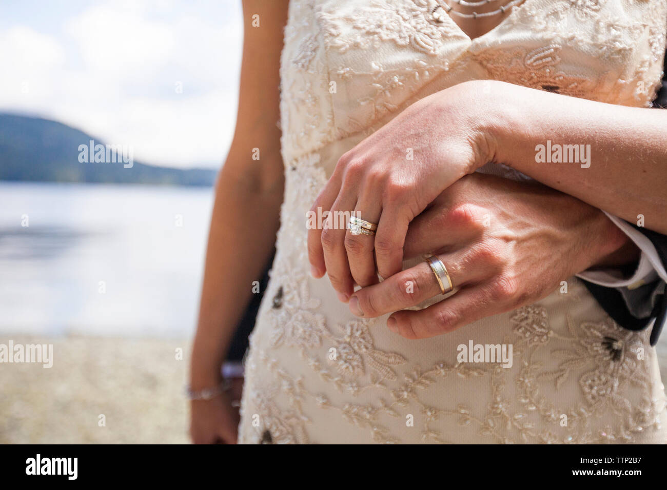 Mittelteil der jungvermählte Paar hält die Hände am Seeufer Stockfoto