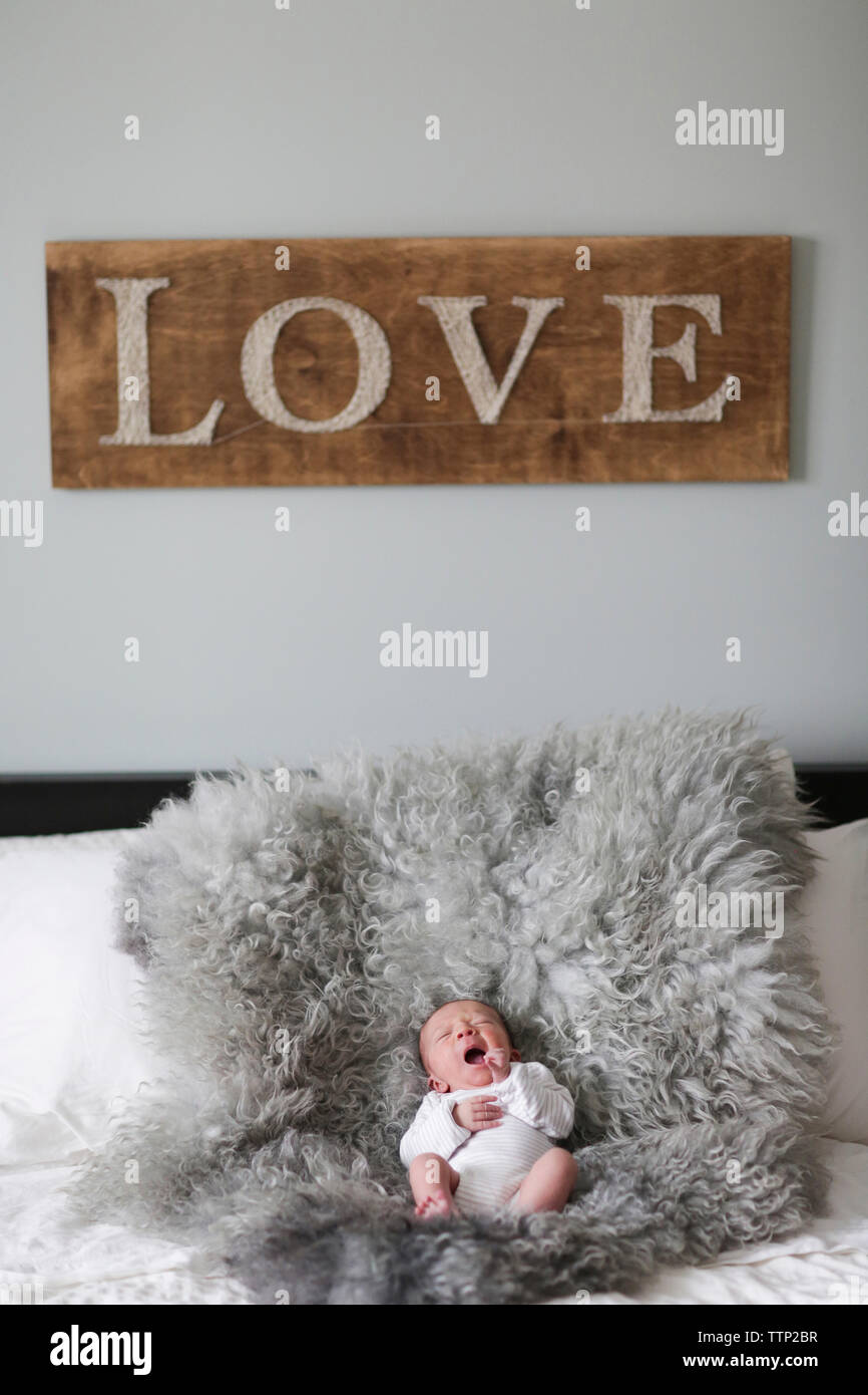 Hohe Betrachtungswinkel von baby boy Gähnen während des Schlafes auf Fell Teppich im Schlafzimmer mit Liebe eingerichtet und an der Wand Stockfoto