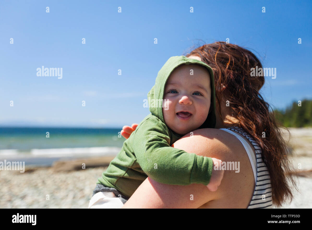 Portrait von baby boy mit Mutter am Strand gegen den blauen Himmel Stockfoto
