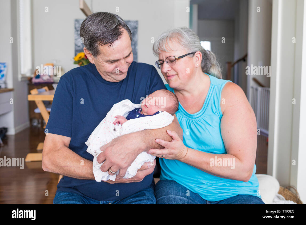 Großeltern mit niedlichen neugeborenen Enkeltochter sitzen im Wohnzimmer zu Hause Stockfoto