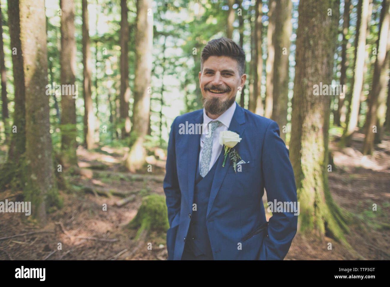 Portrait von glücklichen Bräutigam mit Händen in den Taschen gegen Bäume im Wald Stockfoto