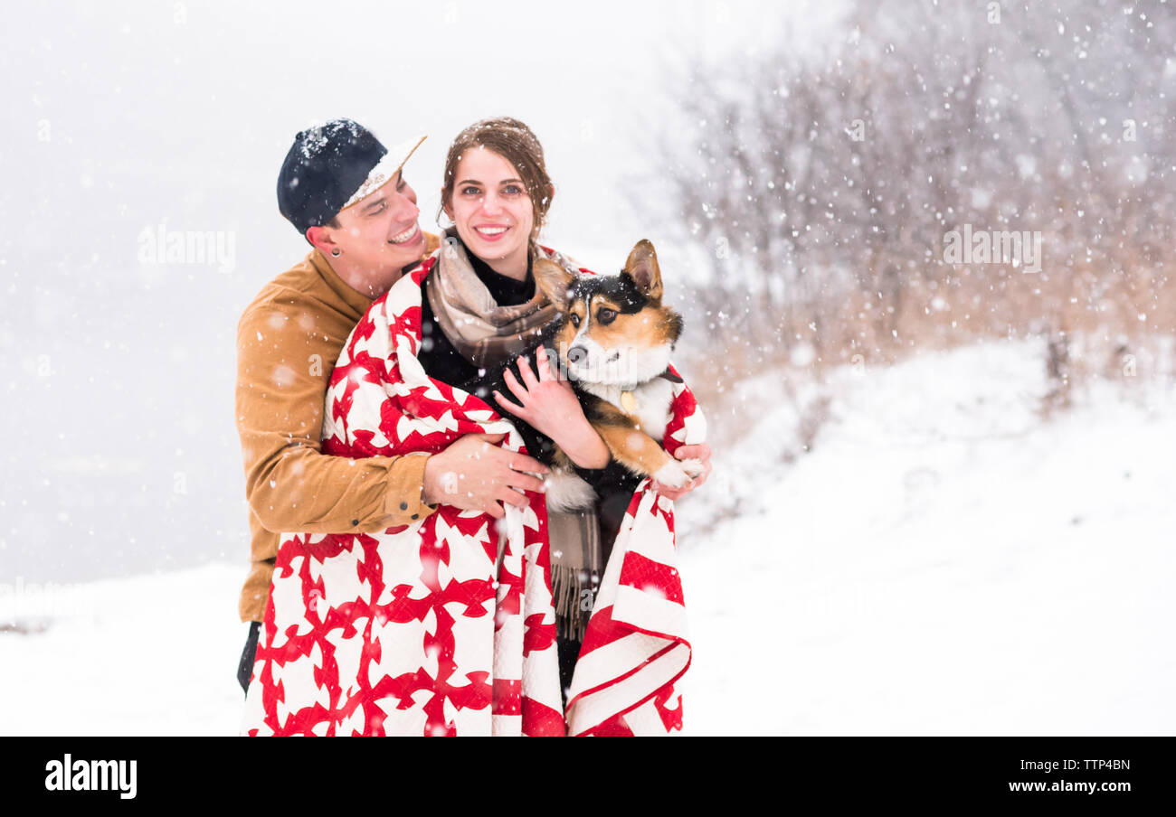 Junges Paar Lächeln und Unordnung bei Schneefall mit Hund Stockfoto