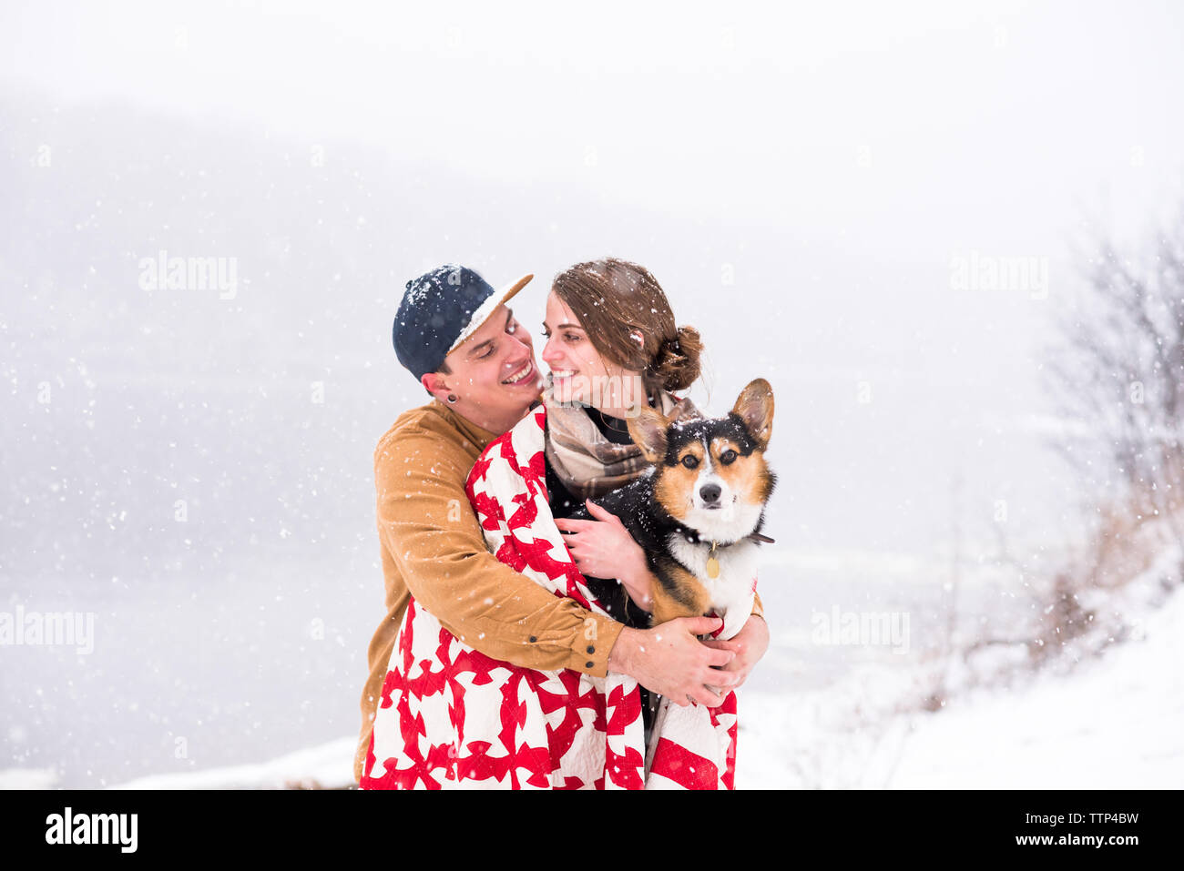 Junges Paar Lächeln und Unordnung bei Schneefall mit Hund Stockfoto