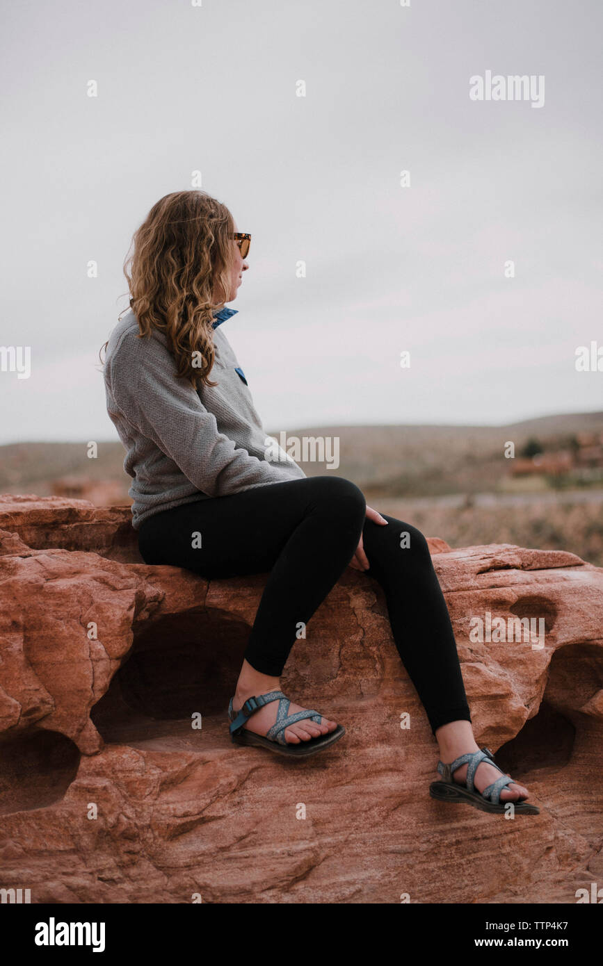 Die ganze Länge der Frau sitzt auf Felsen gegen den Himmel in der Red Rock Canyon National Conservation Area Stockfoto
