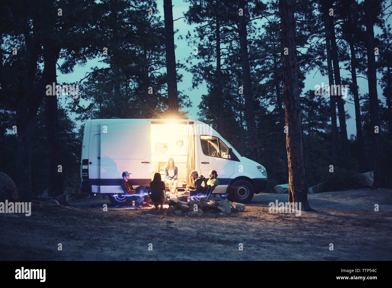 Freunde sprechen während der Sitzung von Motor home im Wald bei Sonnenuntergang Stockfoto