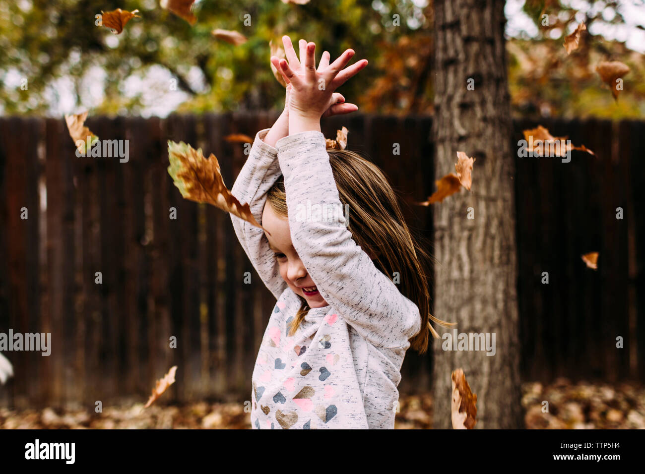 Fröhliches Mädchen spielen mit trockenen Blättern im Park im Herbst Stockfoto