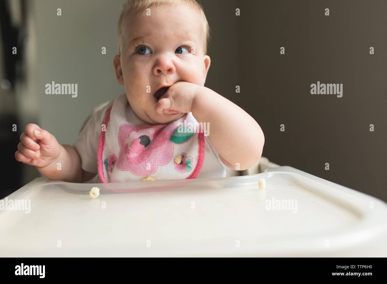 Baby Mädchen mit Finger im Mund sitzen auf hohen Stuhl zu Hause Cute Stockfoto