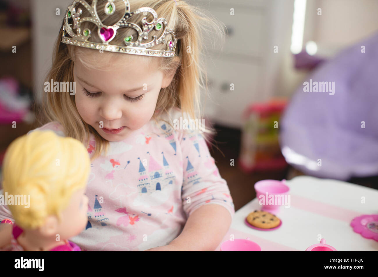 Mädchen mit Krone während des Spielens mit Puppe zu Hause Stockfoto
