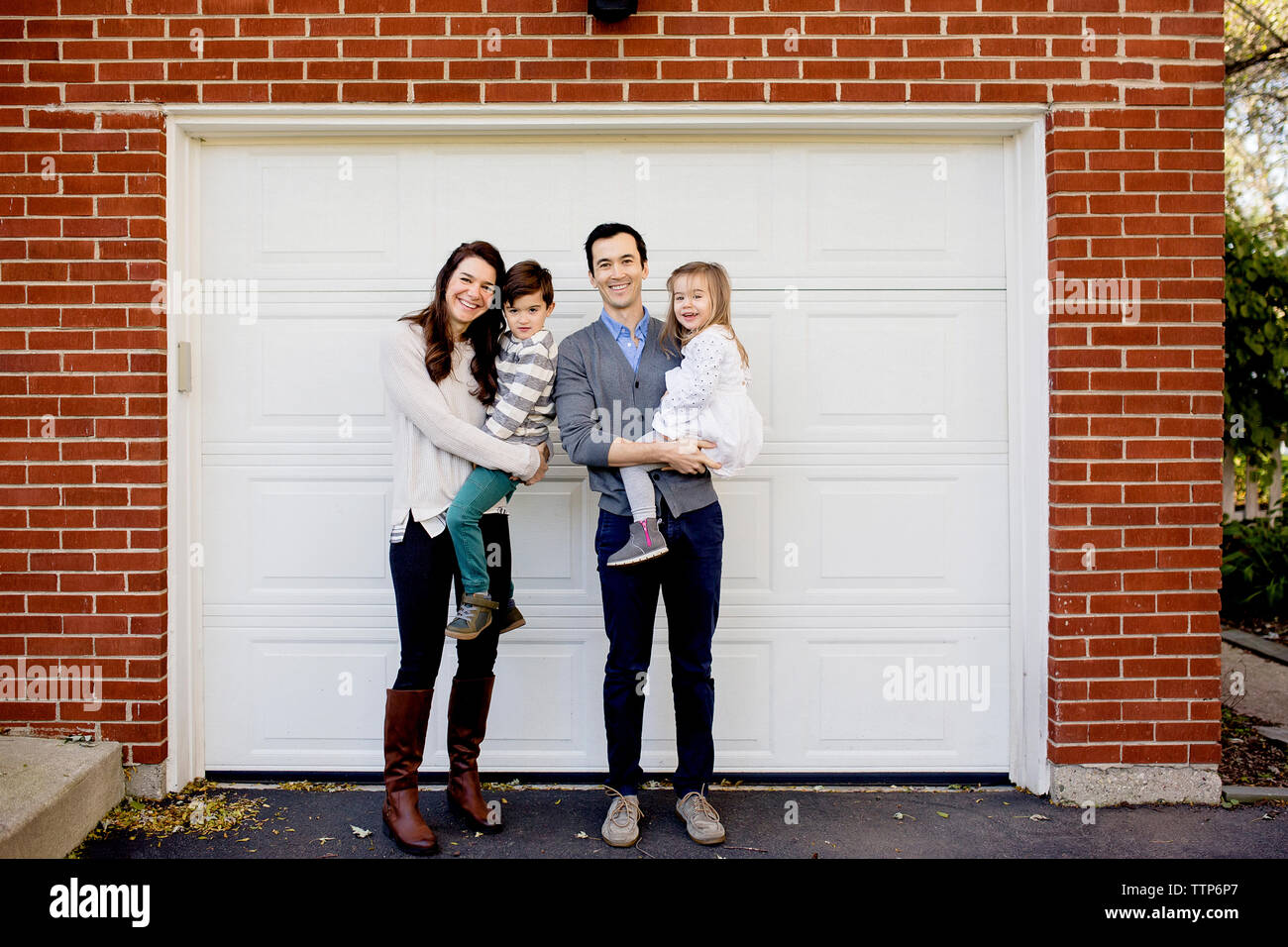 Portrait von glücklichen Eltern Kinder tragen beim Stehen gegen Garage Stockfoto