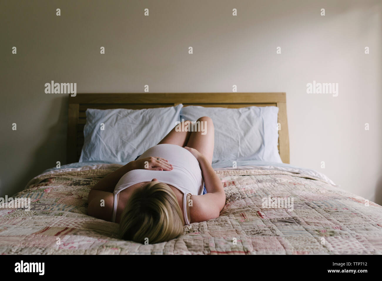 Schwangere Frau liegend auf Bett mit Hände auf Bauch gegen die Wand zu Hause Stockfoto