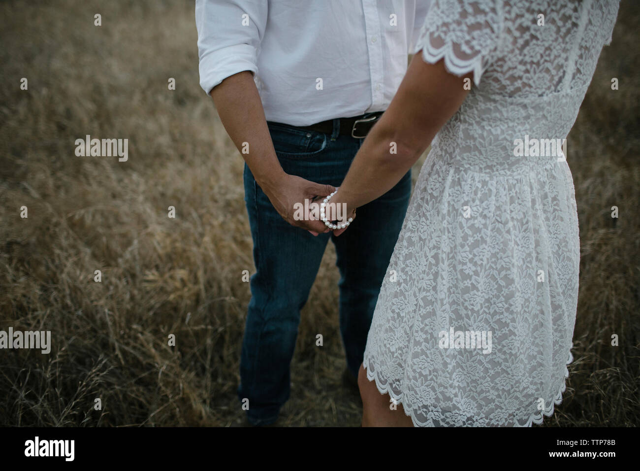 Mittelteil des Paares, die Hand in Hand stehen auf Feld Stockfoto