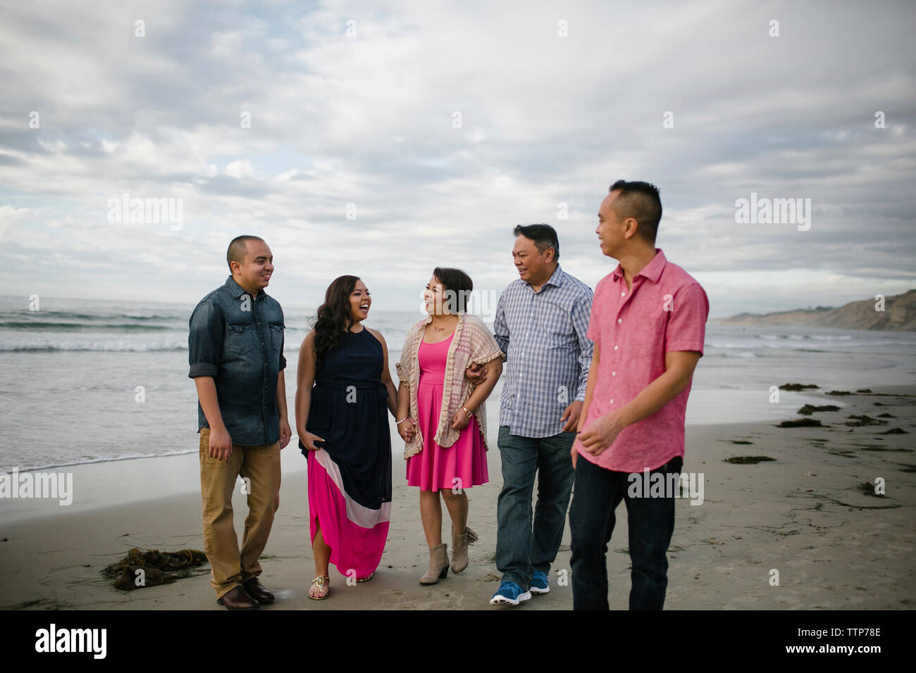 Glückliche Familie zu Fuß auf Ufer am Strand gegen Sky Stockfoto