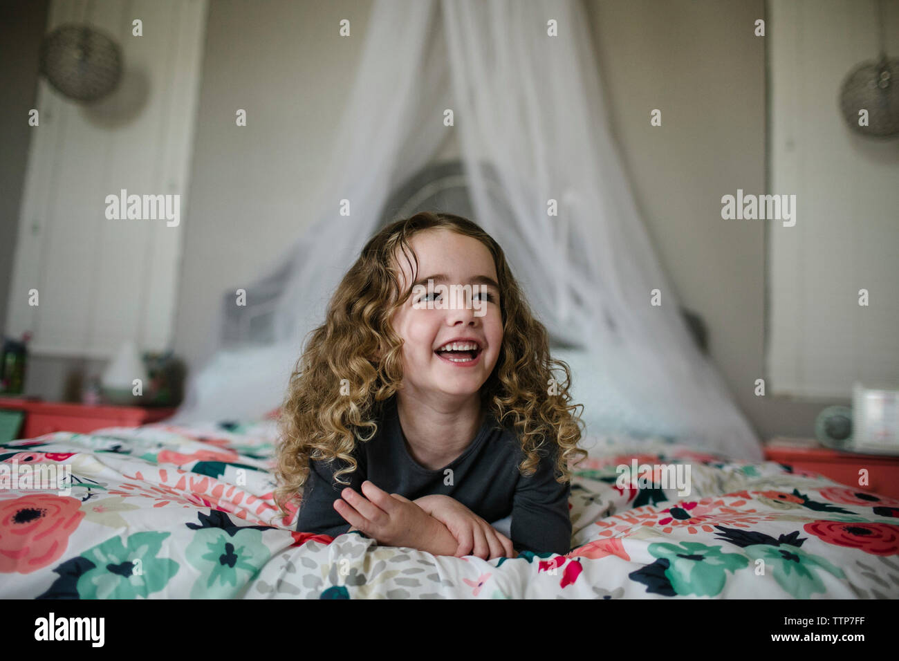 Fröhliches Mädchen weg schauen, während am Bett zu Hause liegen Stockfoto