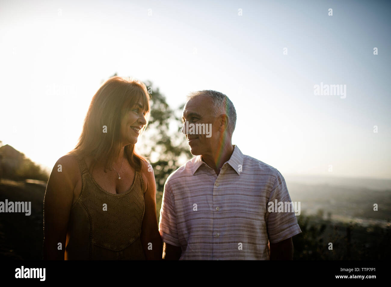 Romantisches Paar sich einander, während gegen den klaren Himmel bei Sonnenuntergang stehend Stockfoto