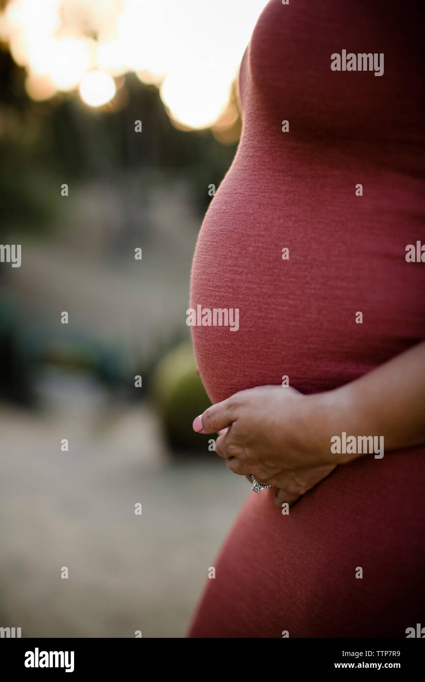 Mittelteil der schwangeren Frau mit Hand auf Magen standing in Park bei Sonnenuntergang Stockfoto