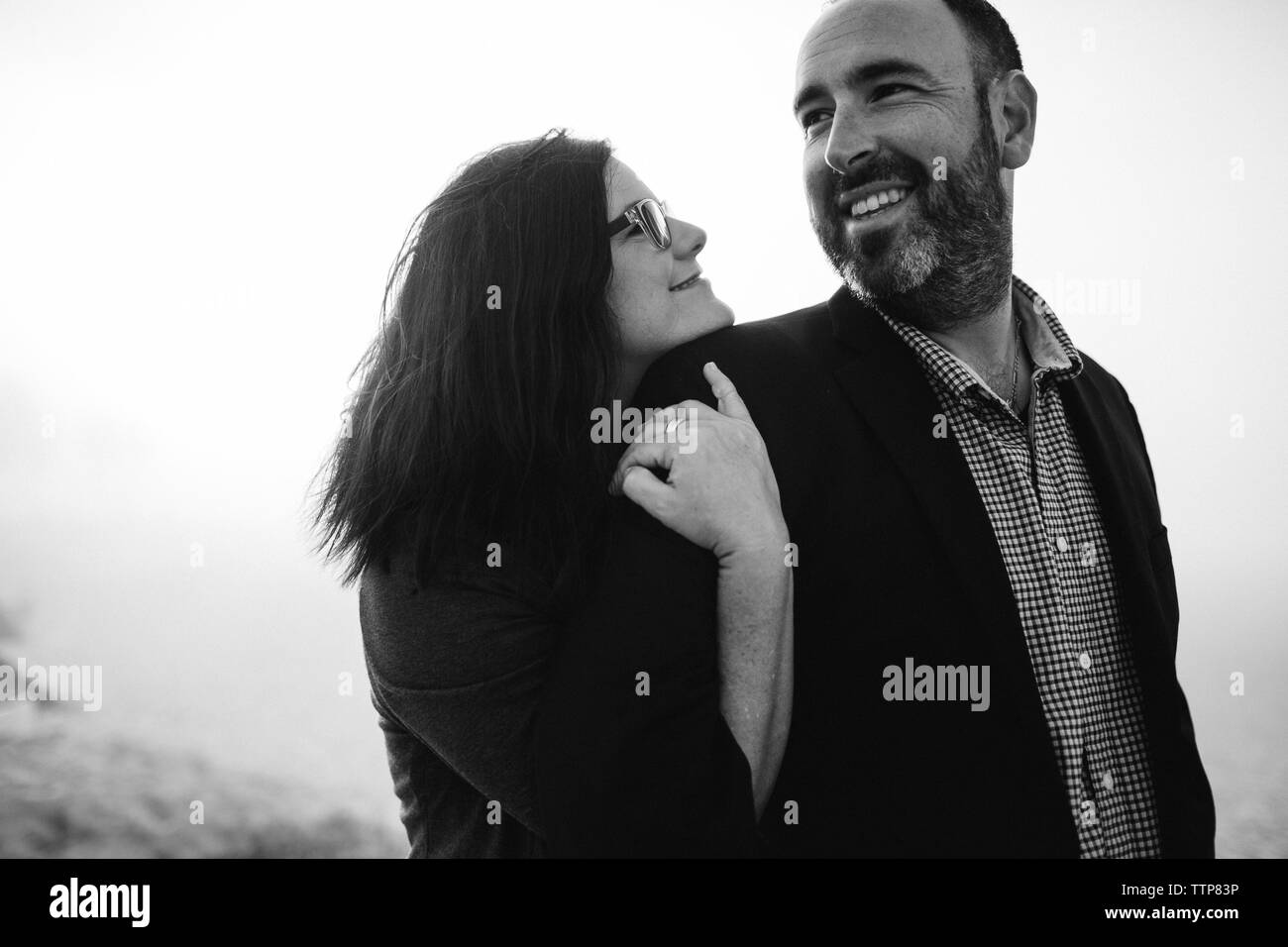 Seitenansicht des glücklichen Paares umarmt, während am Strand während der nebligen Wetter stehend Stockfoto