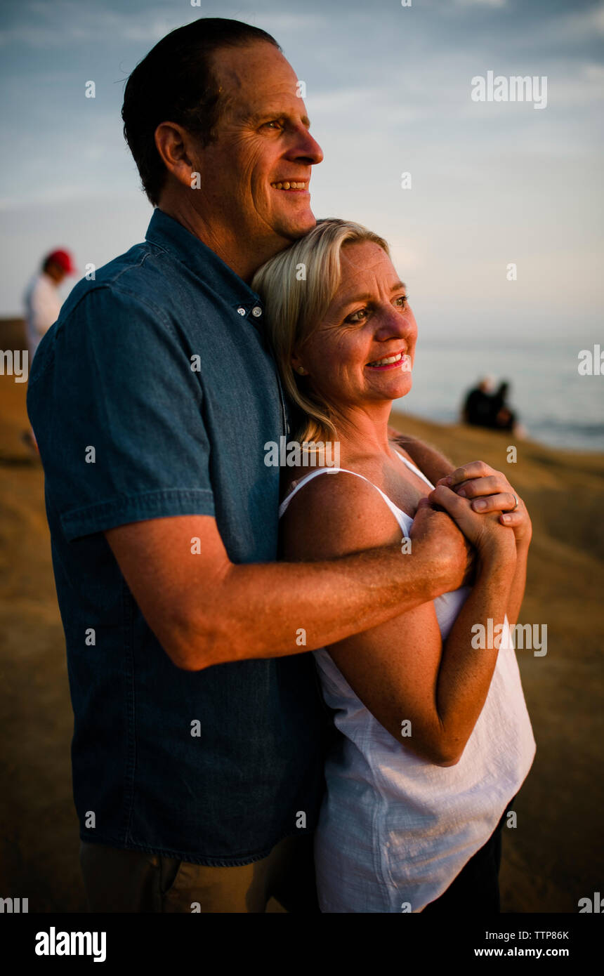 Seitenansicht des Romantisches Paar suchen, während sie sich auf einer Klippe gegen Himmel bei Sonnenuntergang Stockfoto