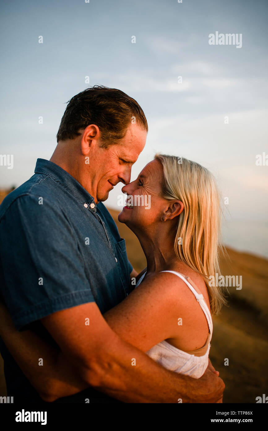 Seitenansicht des Romantisches Paar sich einander beim Stehen auf Klippe gegen Himmel bei Sonnenuntergang Stockfoto