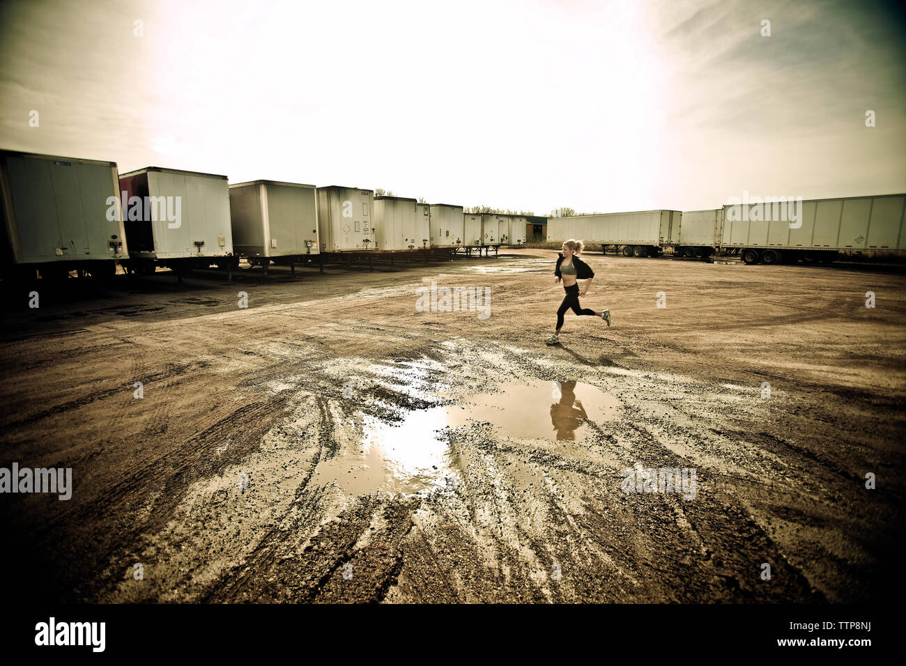 Sportler joggen auf matschigen Feld durch Cargo Container gegen Sky Stockfoto