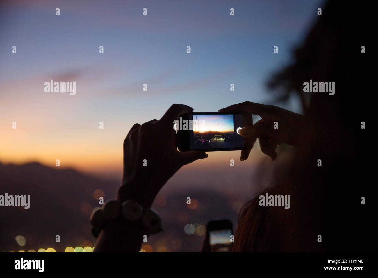 Frau fotografieren beleuchtete Stadtbild mit smart phone bei Sonnenuntergang Stockfoto