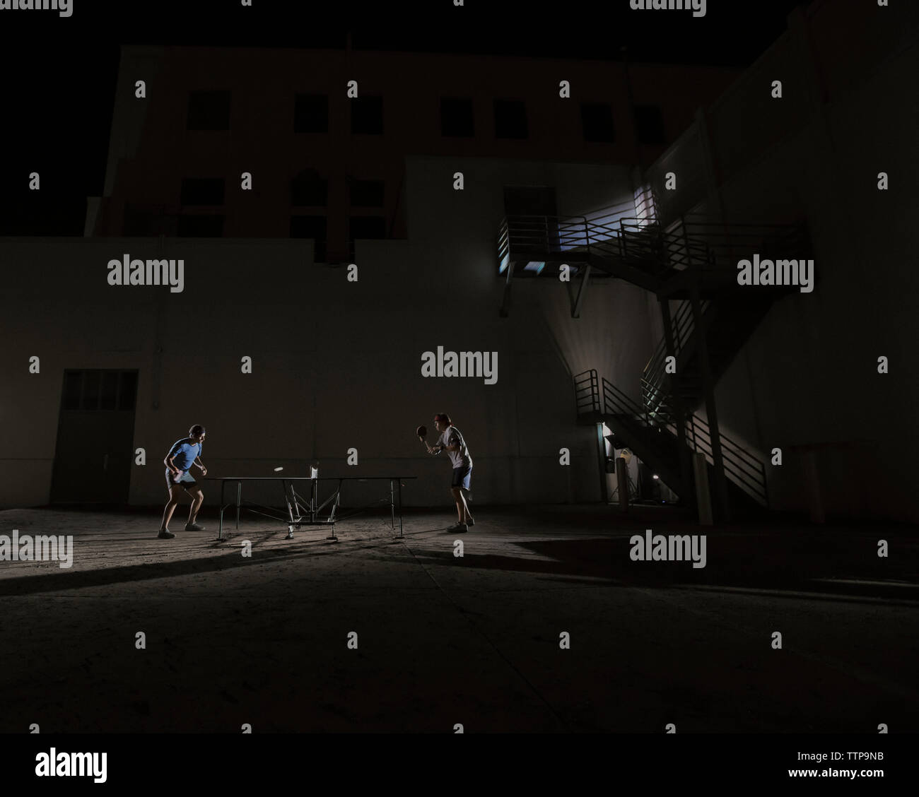 Seitenansicht des männlichen Freunde Tischtennis spielen gegen beleuchtete Gebäude Stockfoto