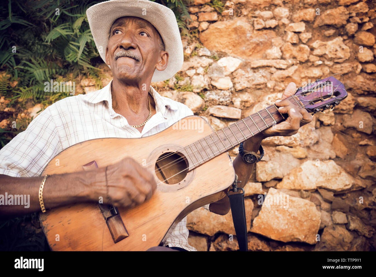 Man Gitarre spielen während der Sitzung gegen die Mauer aus Stein Stockfoto