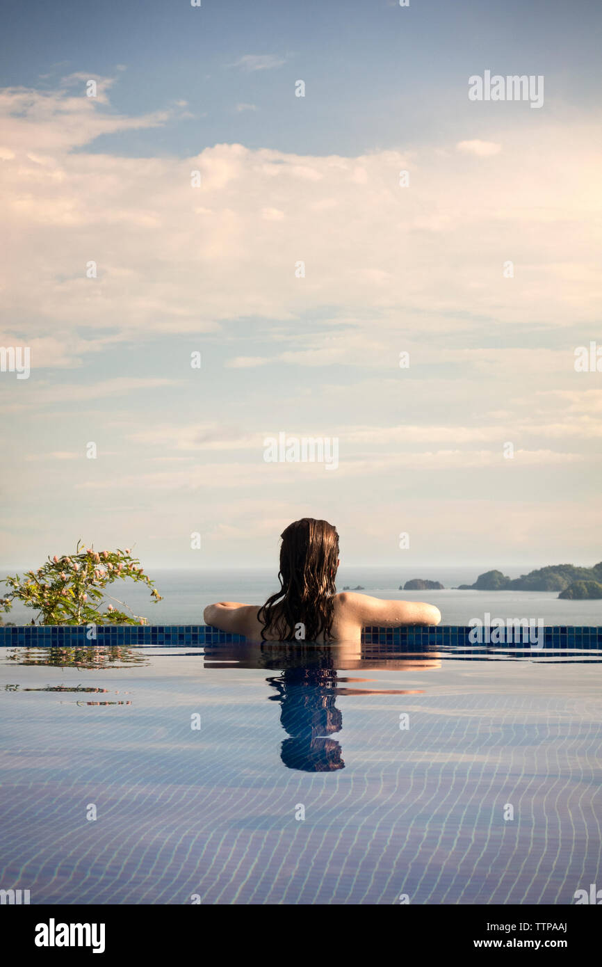Rückansicht der Frau in der Swimmingpool und Blick auf Costa Rica gegen bewölkter Himmel Stockfoto