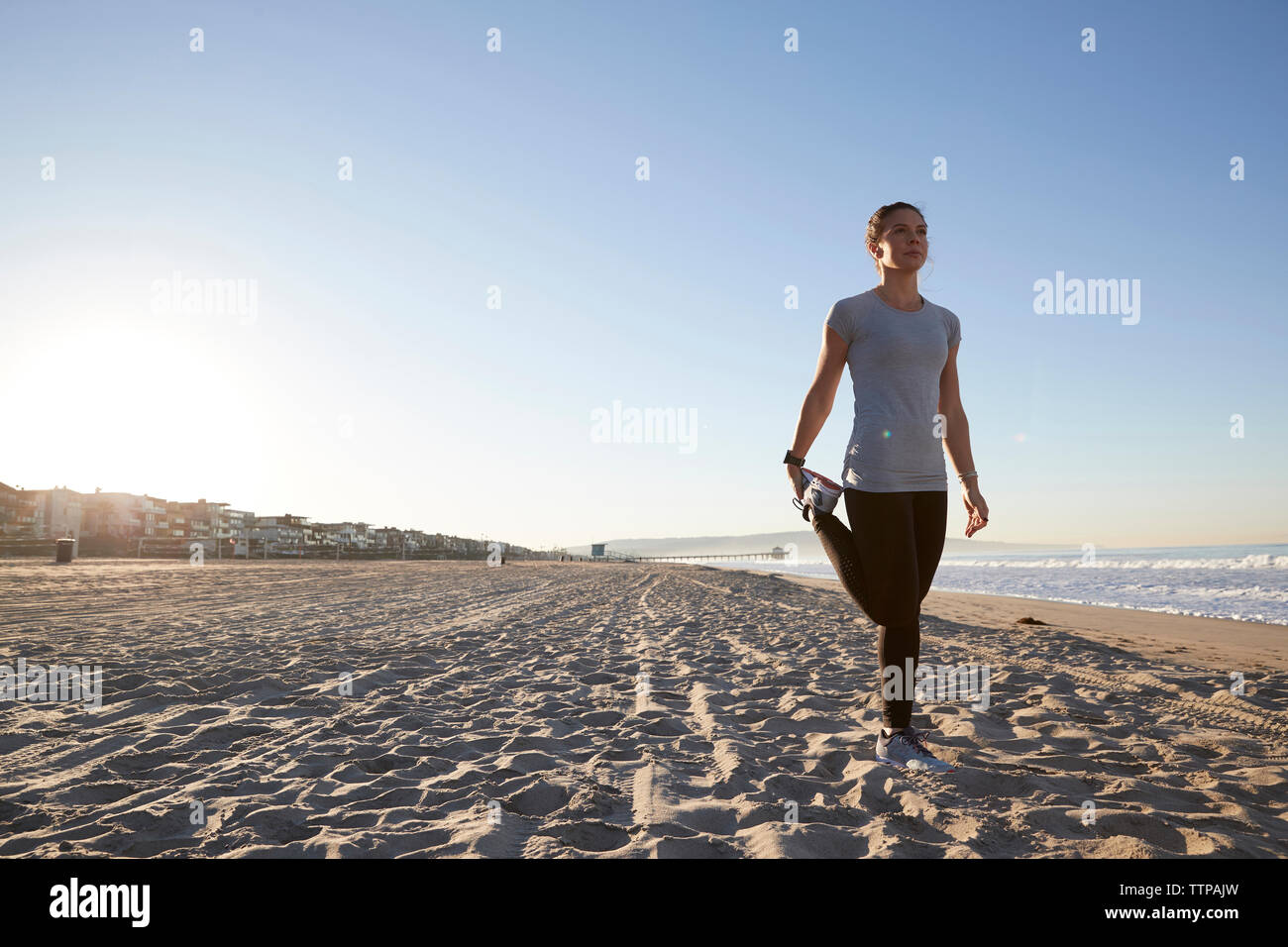 Volle Länge des Frau ausdehnen, während auf einem Bein gegen den klaren Himmel stehen am Strand Stockfoto