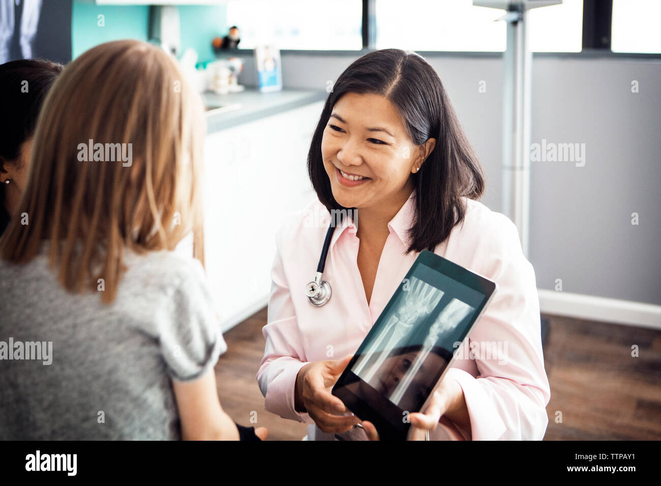 Lächelnd weibliche Arzt Hand zeigt x-ray auf Tablet Computer mit Mädchen in der Klinik Stockfoto