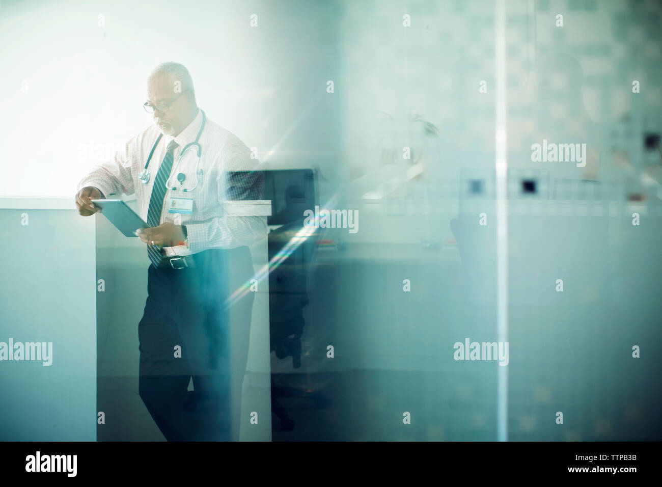 Arzt mit Tablet-PC beim Stehen Krankenhaus Lobby durch Glas gesehen Stockfoto