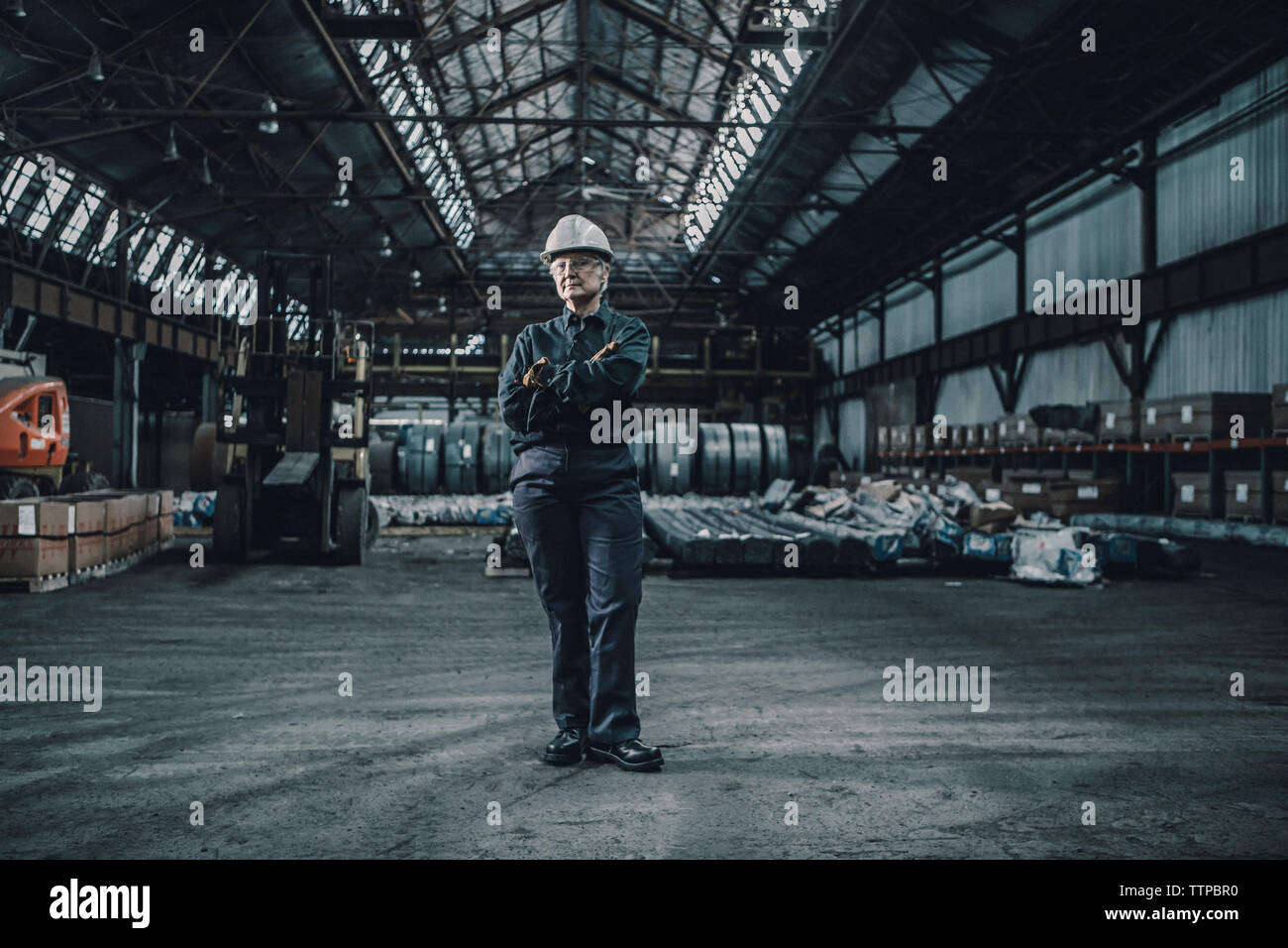 Portrait von zuversichtlich Arbeiterin mit gekreuzten Armen stehen in der Metallindustrie Stockfoto