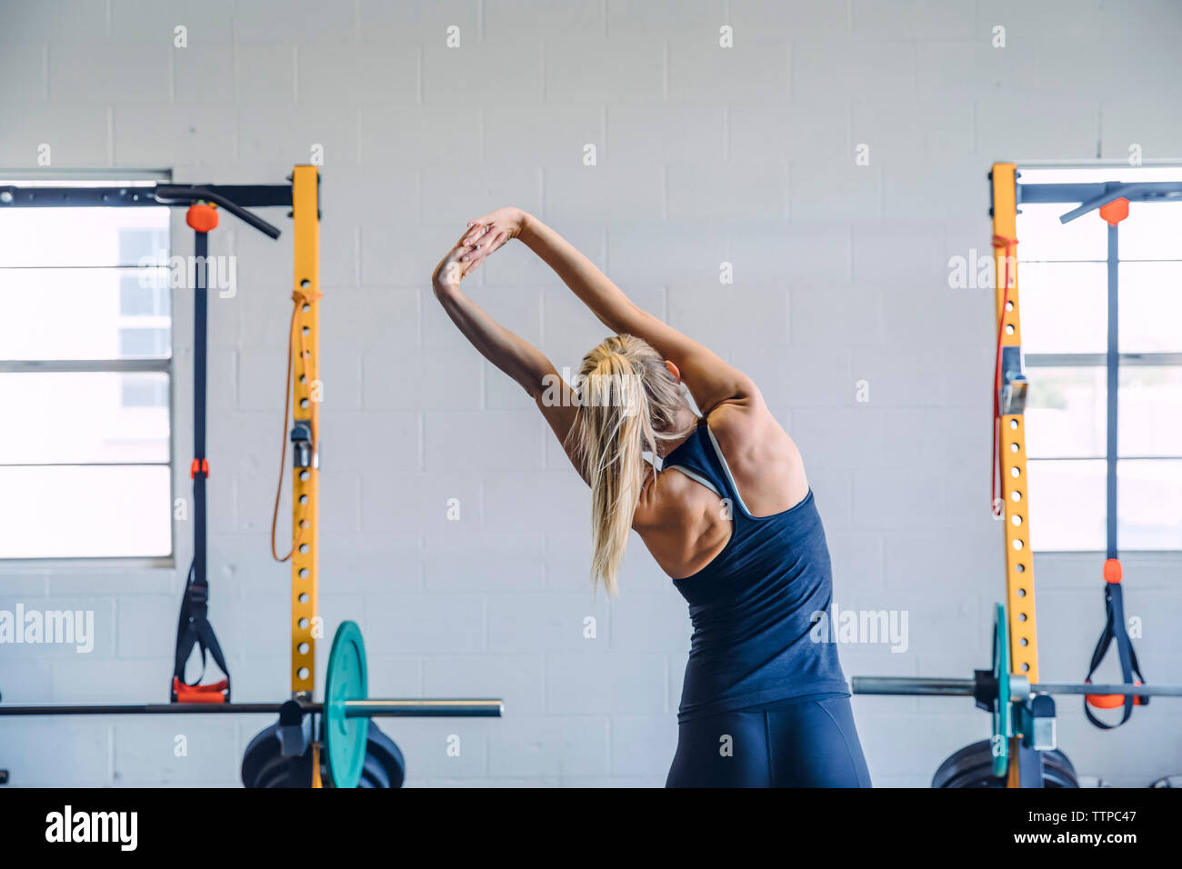 Ansicht der Rückseite Frau mit gefalteten Händen stretching während der Ausübung gegen die Wand in der Turnhalle Stockfoto