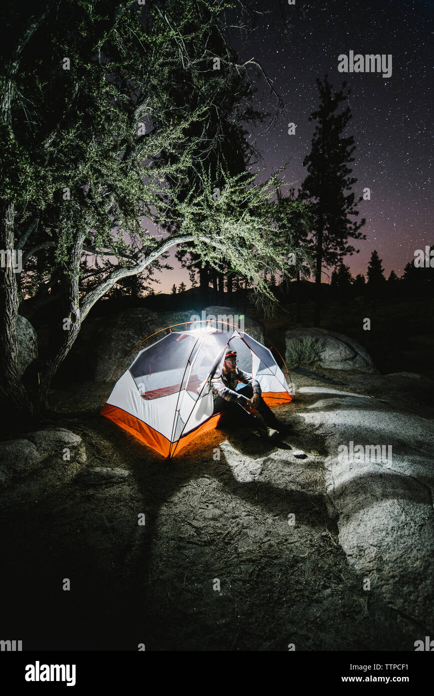 Wanderer sitzen in beleuchteten Zelt auf Rock von Bäumen in der Nacht Stockfoto