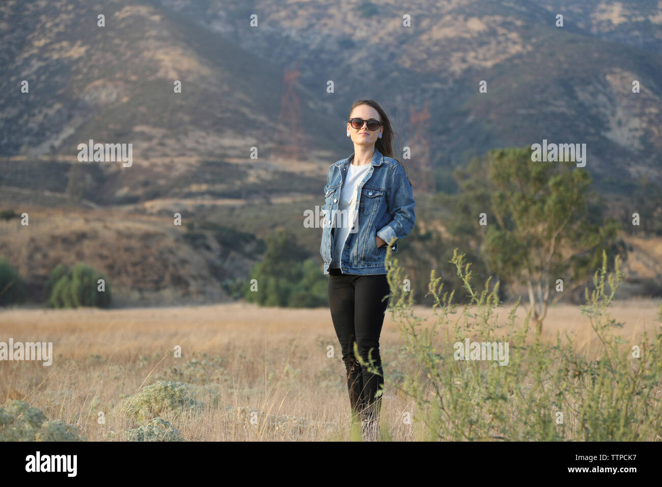 Selbstbewussten jungen Frau mit Händen in den Taschen gegen Berg stehend auf dem Feld Stockfoto