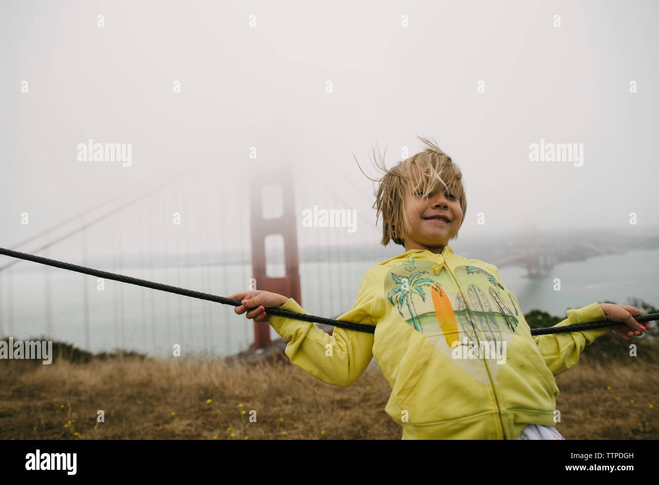 Mädchen lehnte sich auf Kabel gegen Golden Gate Bridge im Nebel Stockfoto