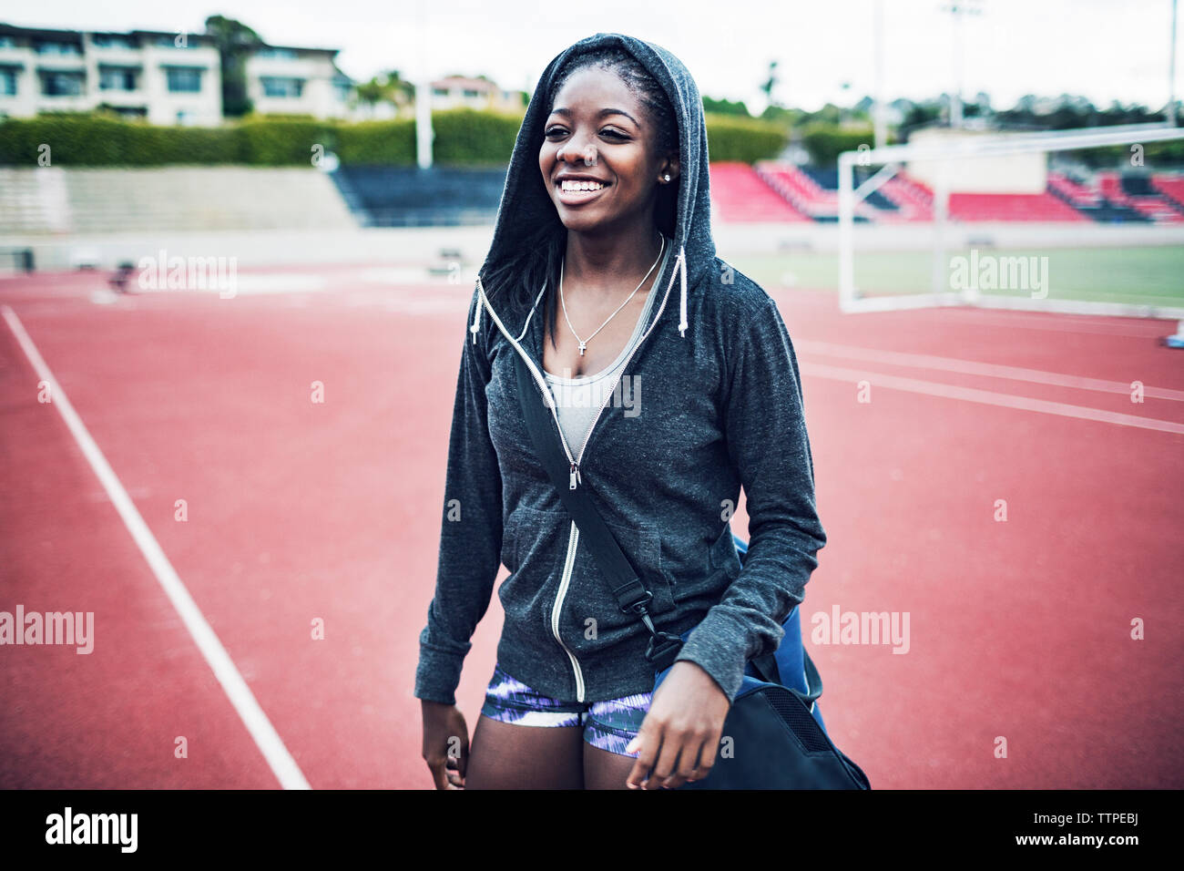Glückliche Athletin in Kapuzenjacke stehend auf Running tracks Stockfoto