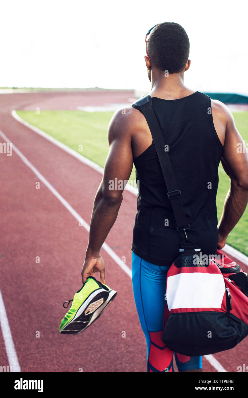 Ansicht der Rückseite des Sportsman holding Sport Schuhe beim Gehen auf Feld Stockfoto