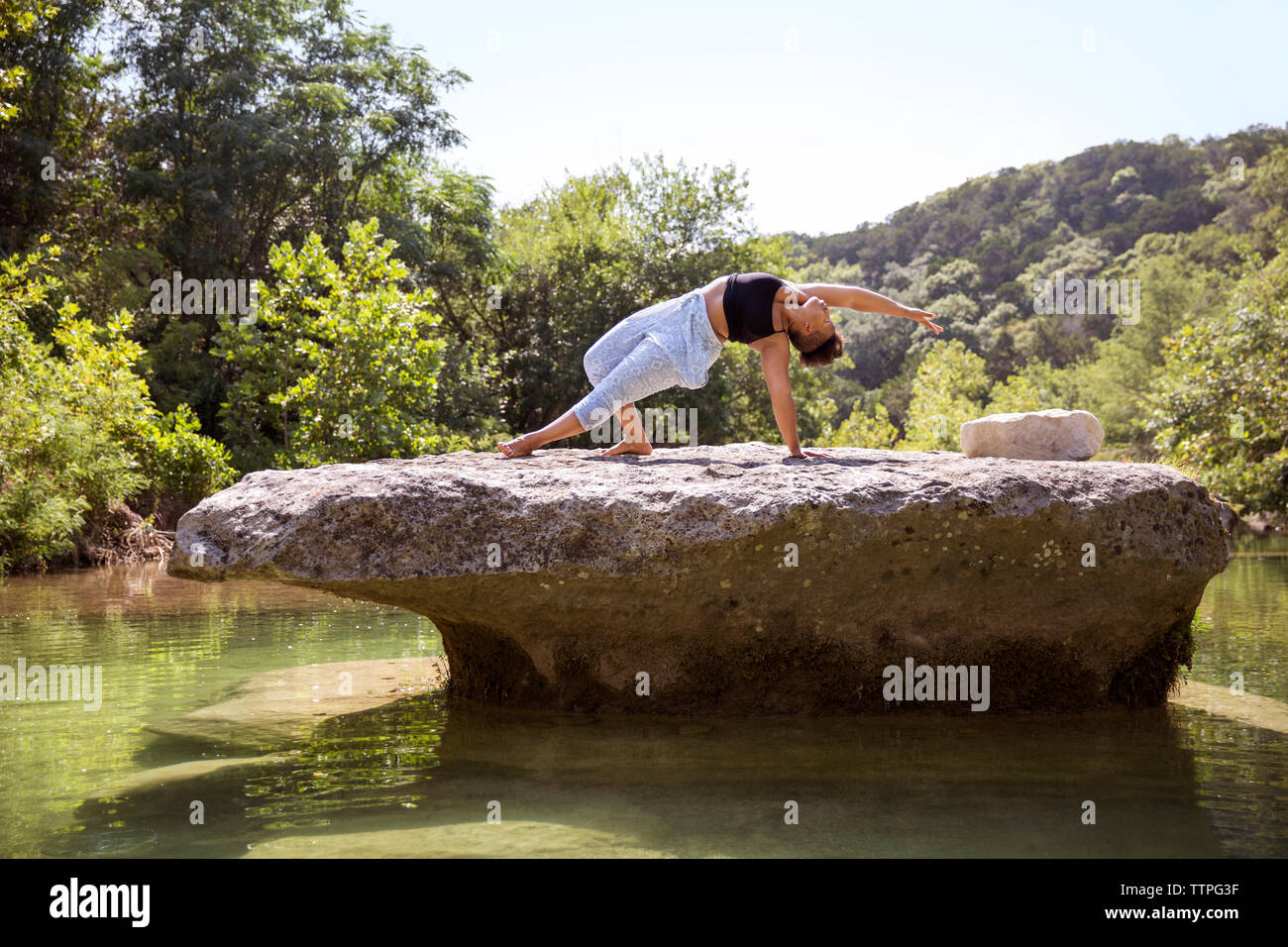 Frau Yoga üben auf Felsen mitten im See am Wald Stockfoto