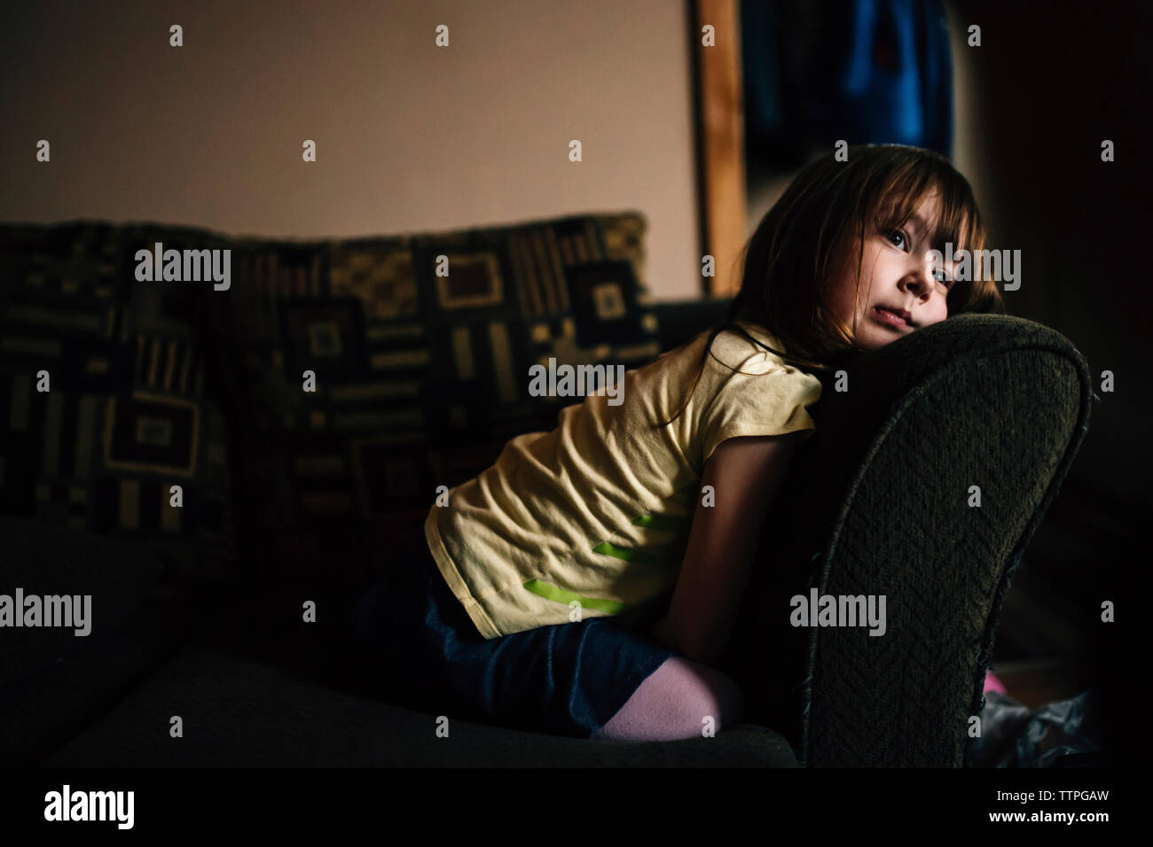 Gelangweilt wegsehen, während Mädchen kniend auf Sofa Stockfoto