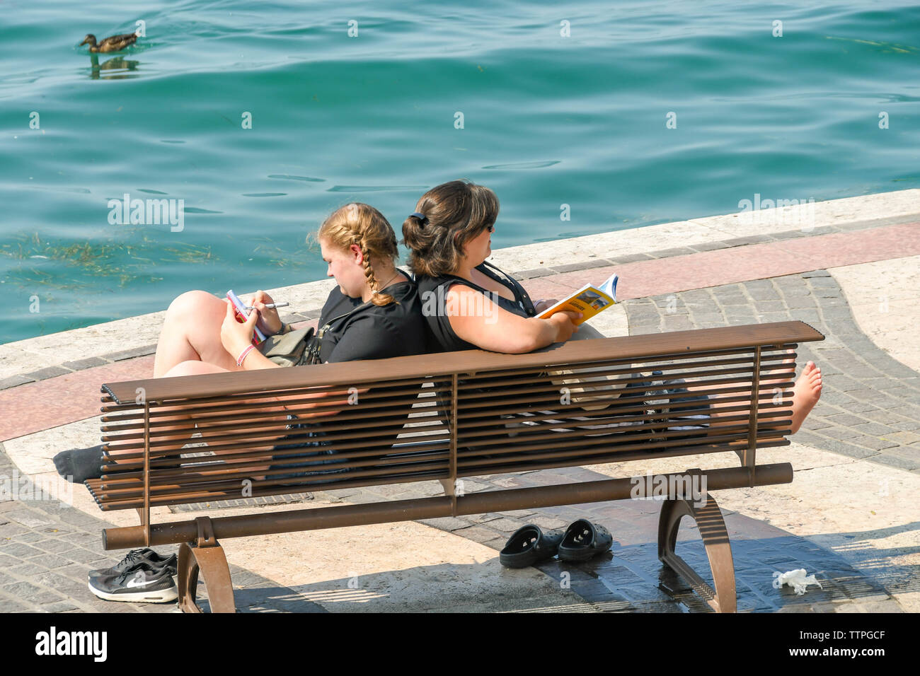 LAZISE, Gardasee, Italien - September 2018: Zwei Personen entspannen auf einer Holzbank, auf der Promenade in Lazise am Gardasee. Stockfoto