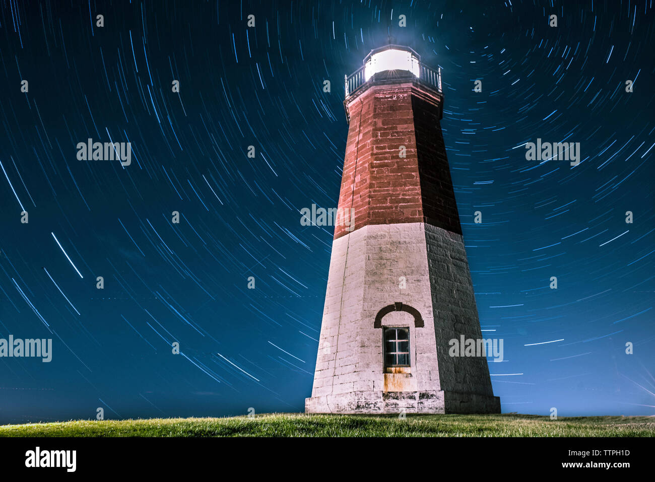 Low Angle Blick auf das beleuchtete Leuchtturm gegen star Trails bei Nacht Stockfoto